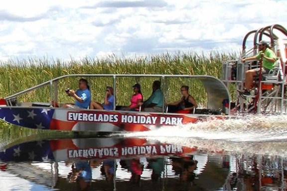 Airboat with passengers on a reflective water surface, Everglades scenery in the background.