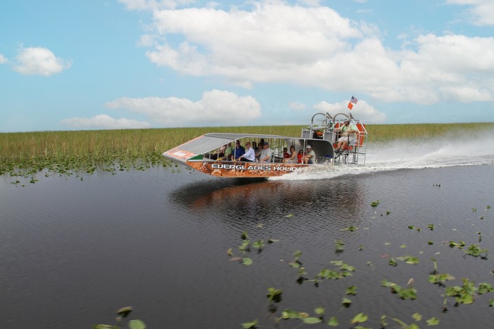Airboat speeding through a marsh with people aboard on a sunny day.