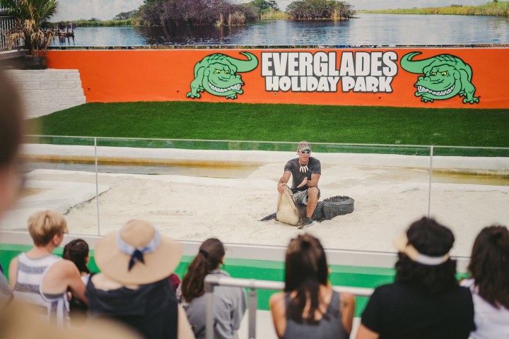 Man sitting on alligator in front of audience at Everglades Holiday Park.