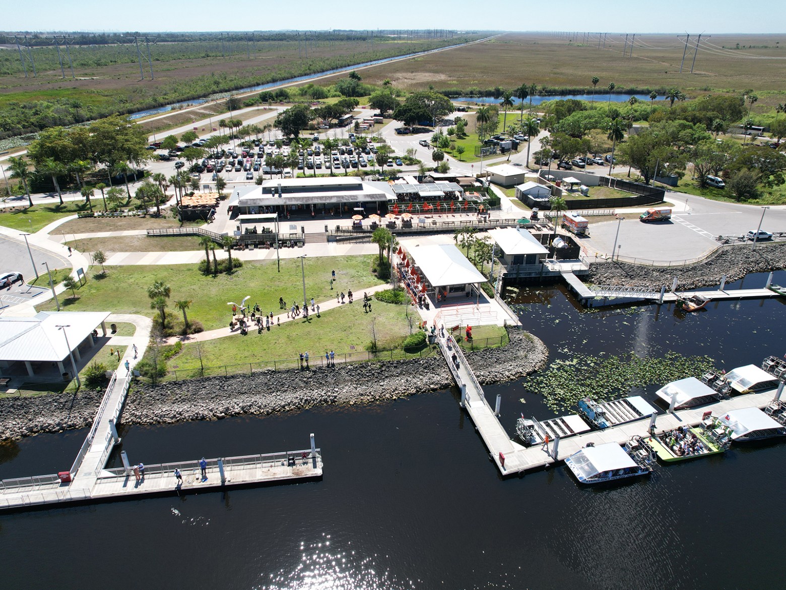 Aerial view of waterfront park with walkways, boats, and parking lot.