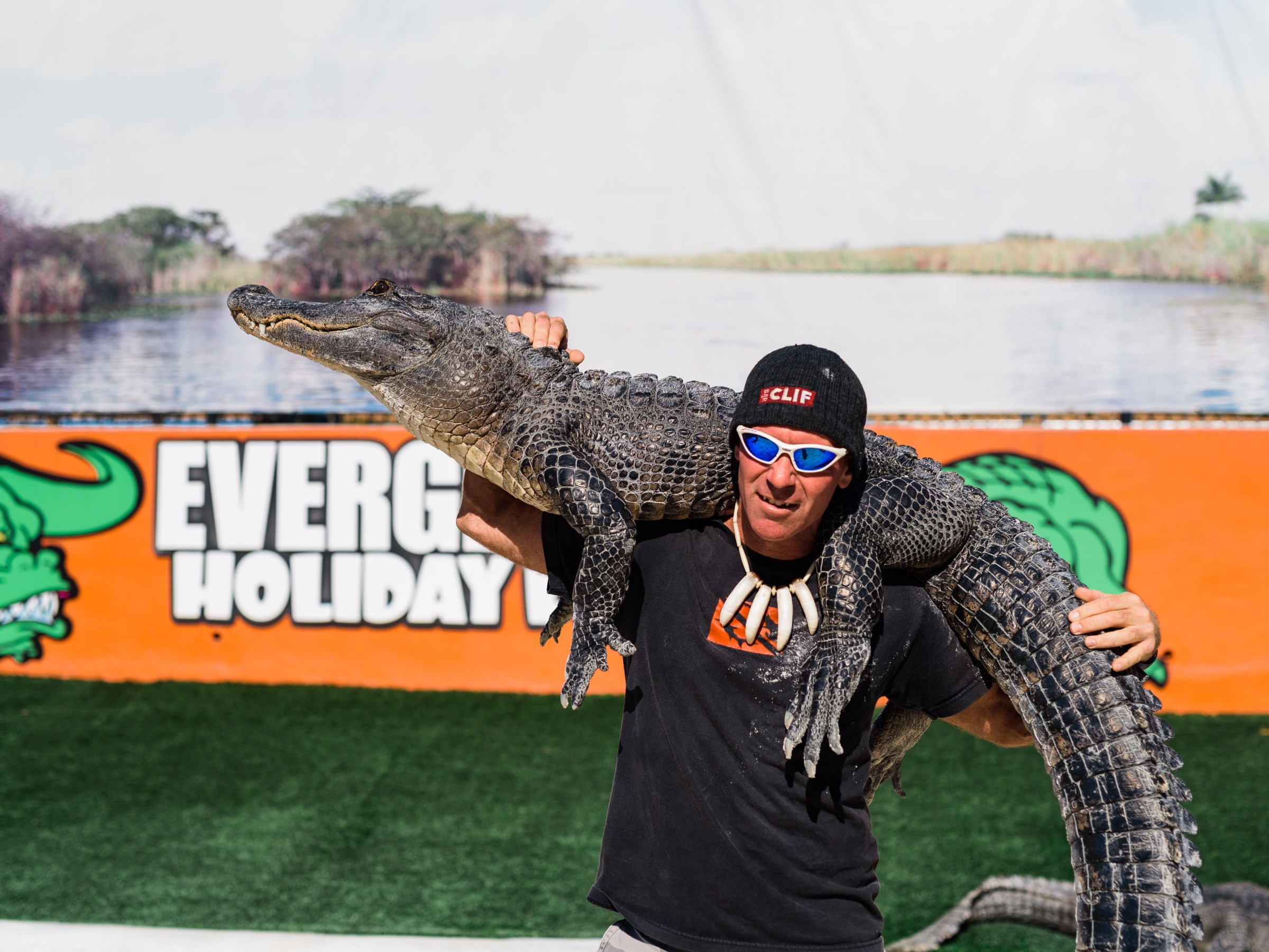 Man holding alligator with background of a sign and landscape.