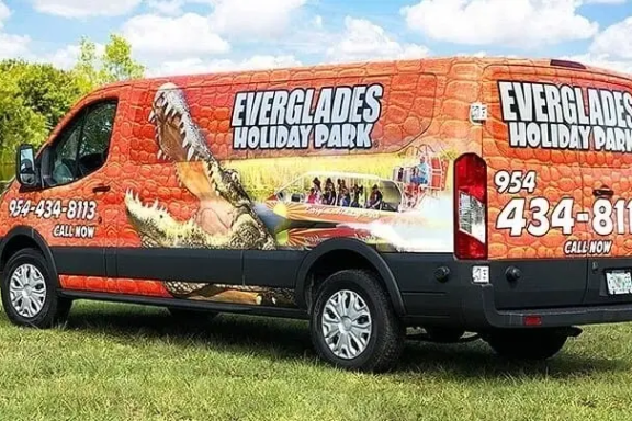 Van with Everglades Holiday Park ad, featuring alligator imagery, parked on grass.