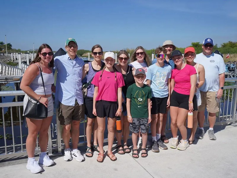 Group of people posing outdoors in sunny weather by a railing.