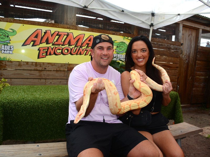 Two people holding a large snake at an outdoor animal encounter exhibit.