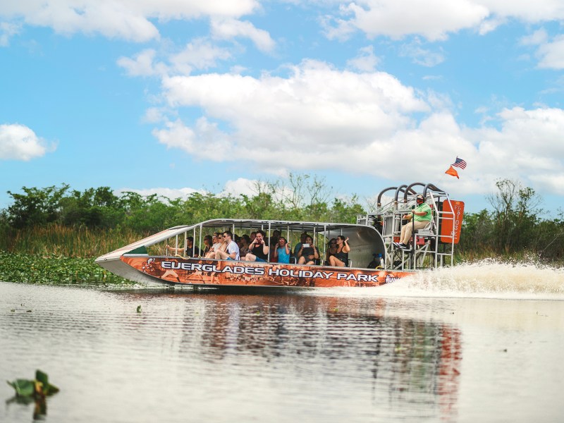 Airboat with passengers on water, American flag flying, clear sky.